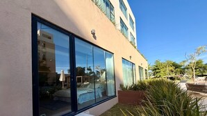 En moderne bygning med store vinduer, et synligt interiør med seng og spiseplads, samt en velholdt have med beplantning.