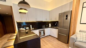 Et moderne køkken med en central ø, integreret hårde hvidevarer og en grå sofa i opholdsområdet.