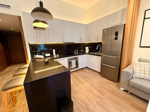 Une cuisine moderne avec un îlot central, des appareils électroménagers intégrés et un canapé gris dans l’espace salon.