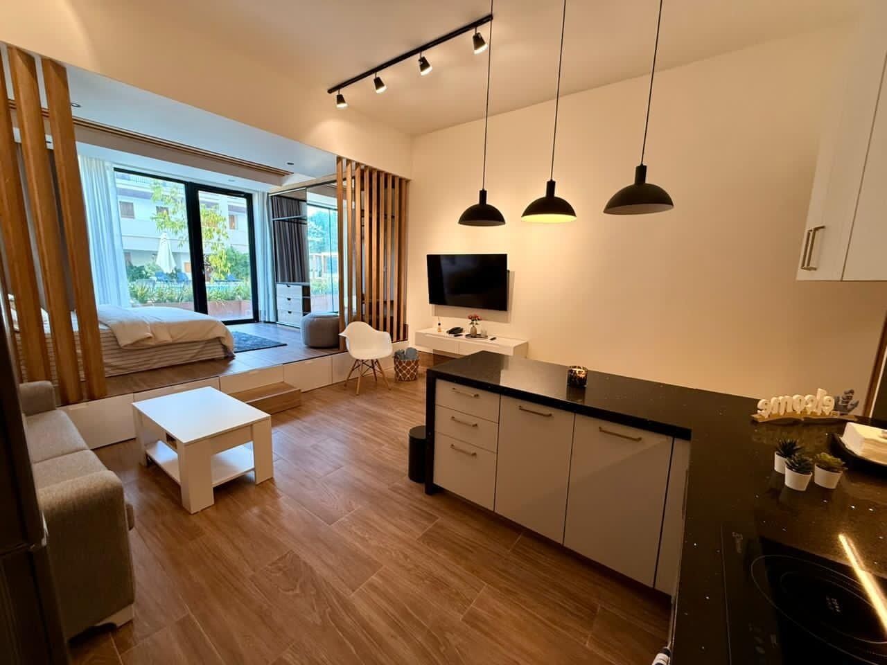 Un salon moderne avec un canapé, une table basse et un téléviseur. Il y a également un coin cuisine équipé de placards et d’un plan de travail.