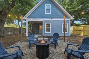 Ein Haus mit überdachter Veranda, Sitzgelegenheiten im Freien und einer Feuerstelle.