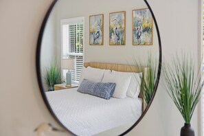 Ein Schlafzimmer mit einem Bett, einem Nachttisch, einer Lampe, einem Spiegel und drei an der Wand befestigten Bildern.