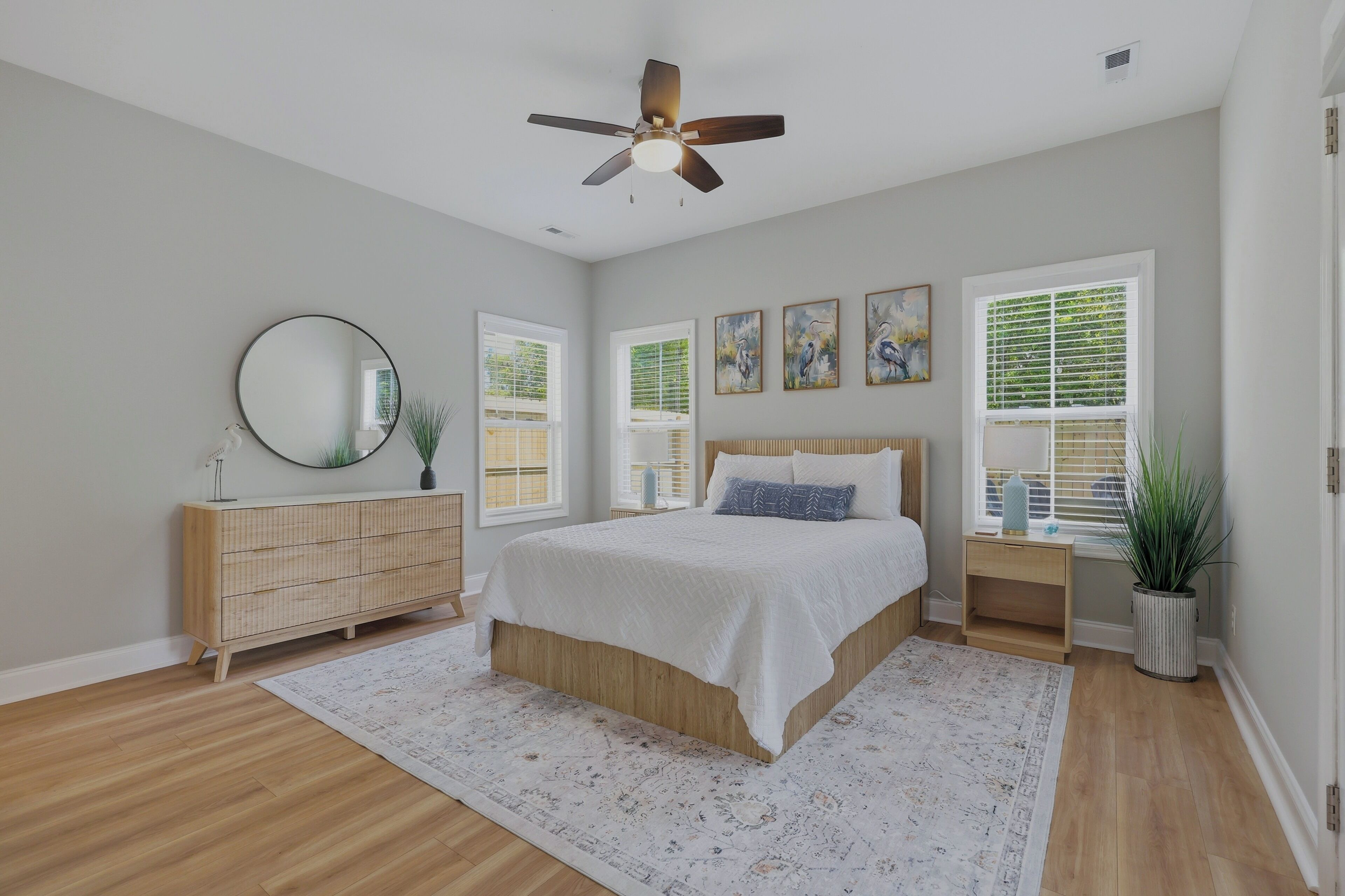 A bedroom with a bed, a ceiling fan, a dresser, a mirror, and artwork on the wall.