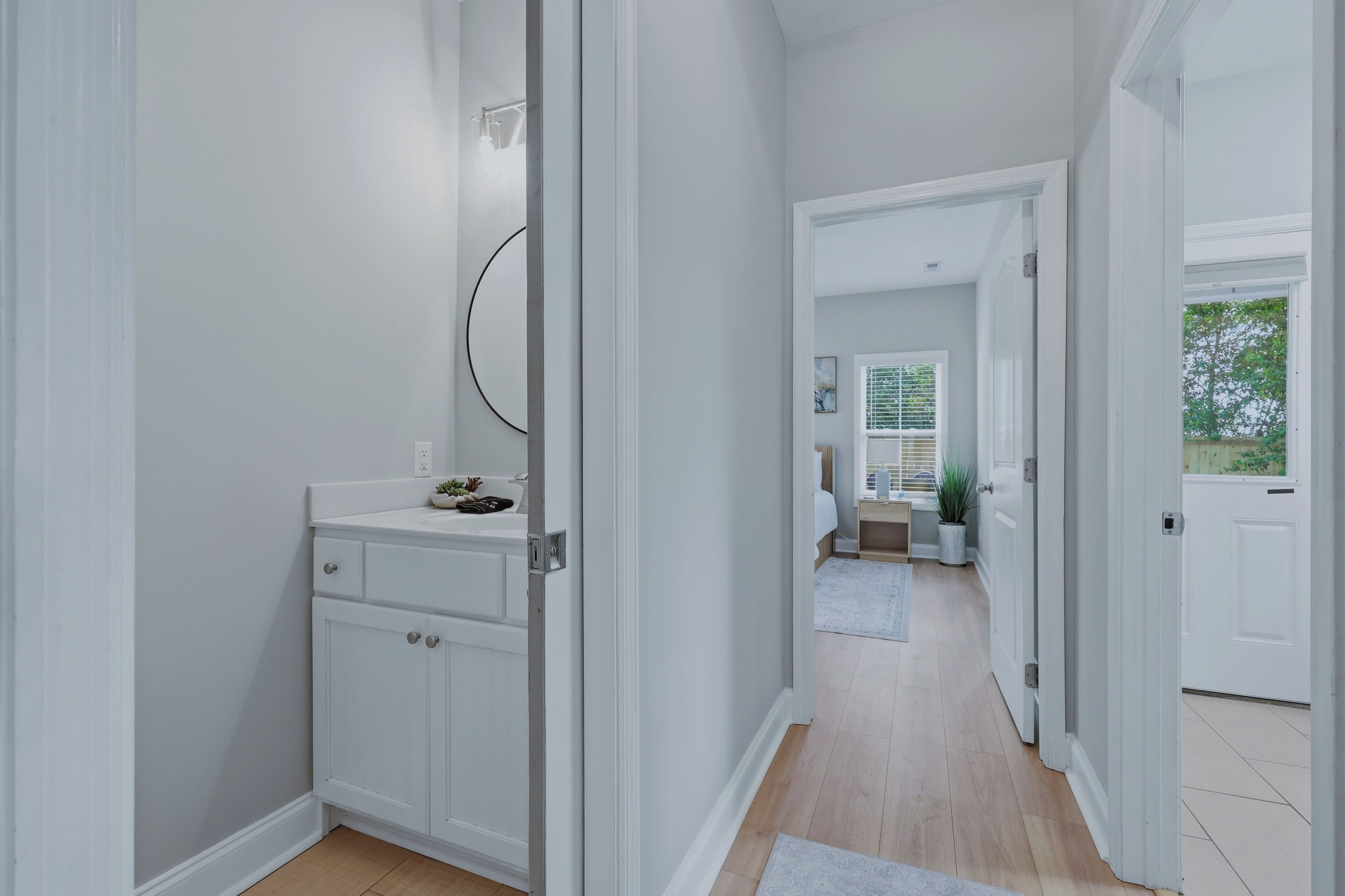 A hallway with a white door leading to a bathroom with a sink and cabinets.