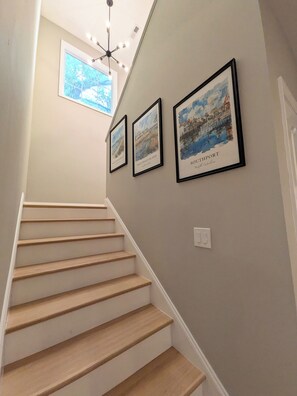 Eine Treppe mit Holzbodenstufen und einer hellen Wand. Drei gerahmte Bilder hängen an der Wand, jedes zeigt einen anderen Ort.