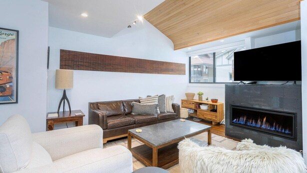 A modern living room with a leather sofa, a white armchair, a coffee table, a fireplace, and a television mounted on the wall. - Telluride Lodge Condo 323 (Telluride)