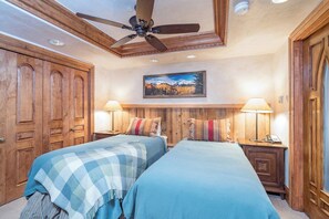 A bedroom with two beds, wooden wardrobe, ceiling fan, wall-mounted lamps, and a painting. - Penthouse At The Peaks 744 (Mountain Village)