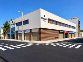 Hotel moderno com fachada plana, várias lojas incluindo uma cafeteria, e uma faixa de pedestres bem definida.