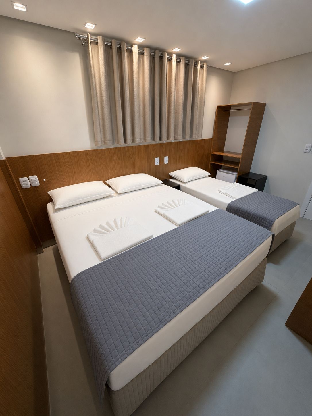 Habitación de hotel con dos camas, un cabecero de madera, un espejo y una mesita de noche pequeña.
