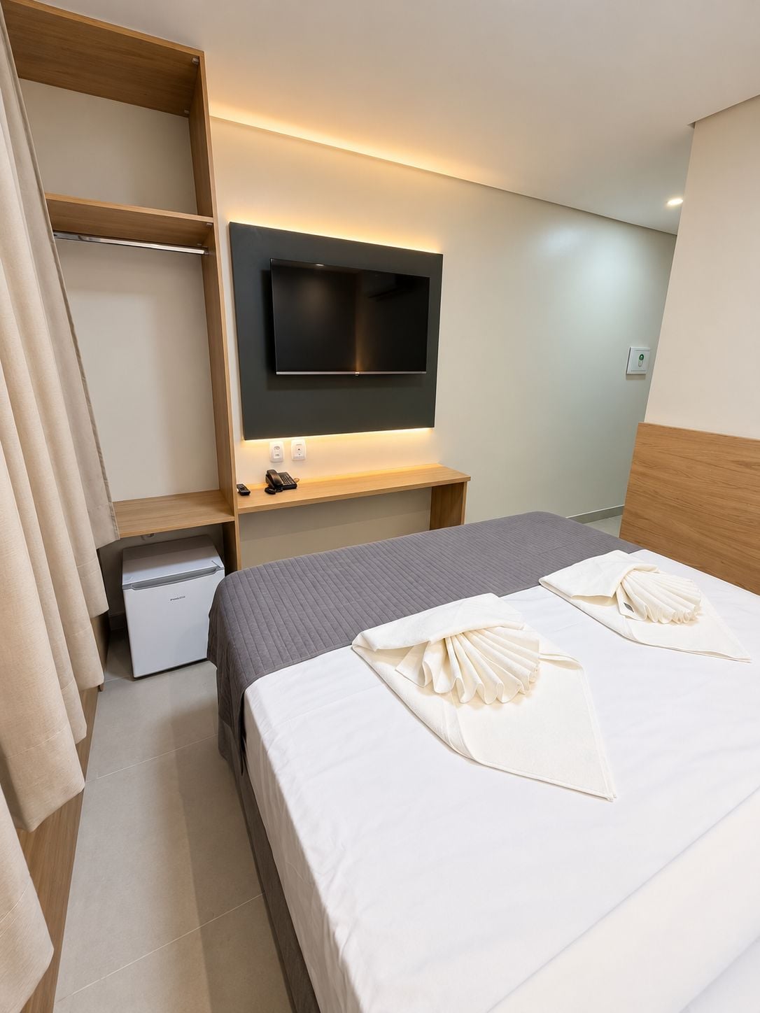 Habitación de hotel con cama, escritorio con televisor de pantalla plana, mini refrigerador y estante empotrado.