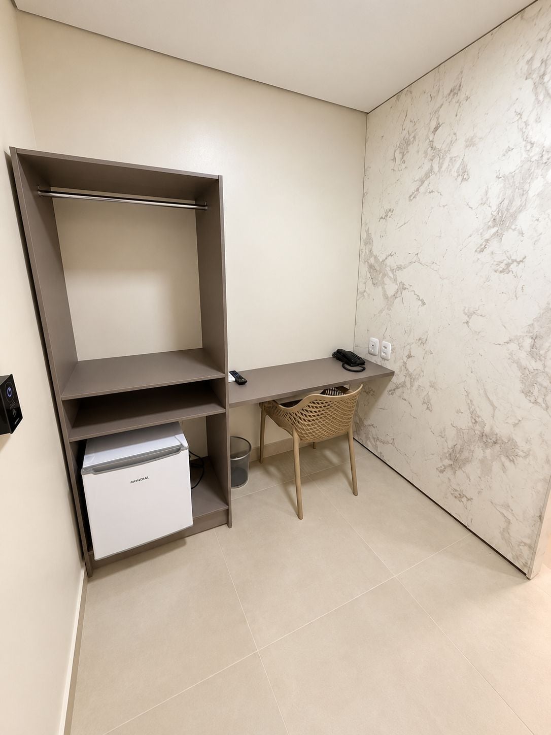 Una habitación pequeña con escritorio, una silla, un electrodoméstico blanco y un estante en la pared.
