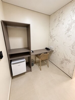 A compact room with a desk, a chair, a small white appliance, and a wall-mounted shelf.