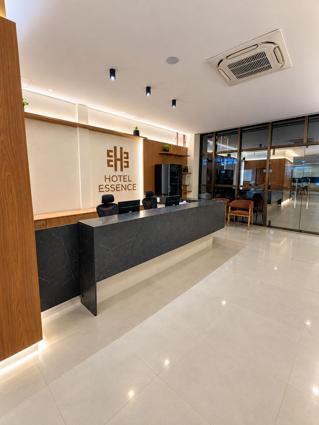 Un mostrador de recepción de hotel con diseño moderno, una pantalla digital y una zona de estar con vistas al interior.