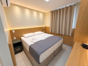 Una habitación de hotel moderna con una cama, mesitas de noche y un climatizador.