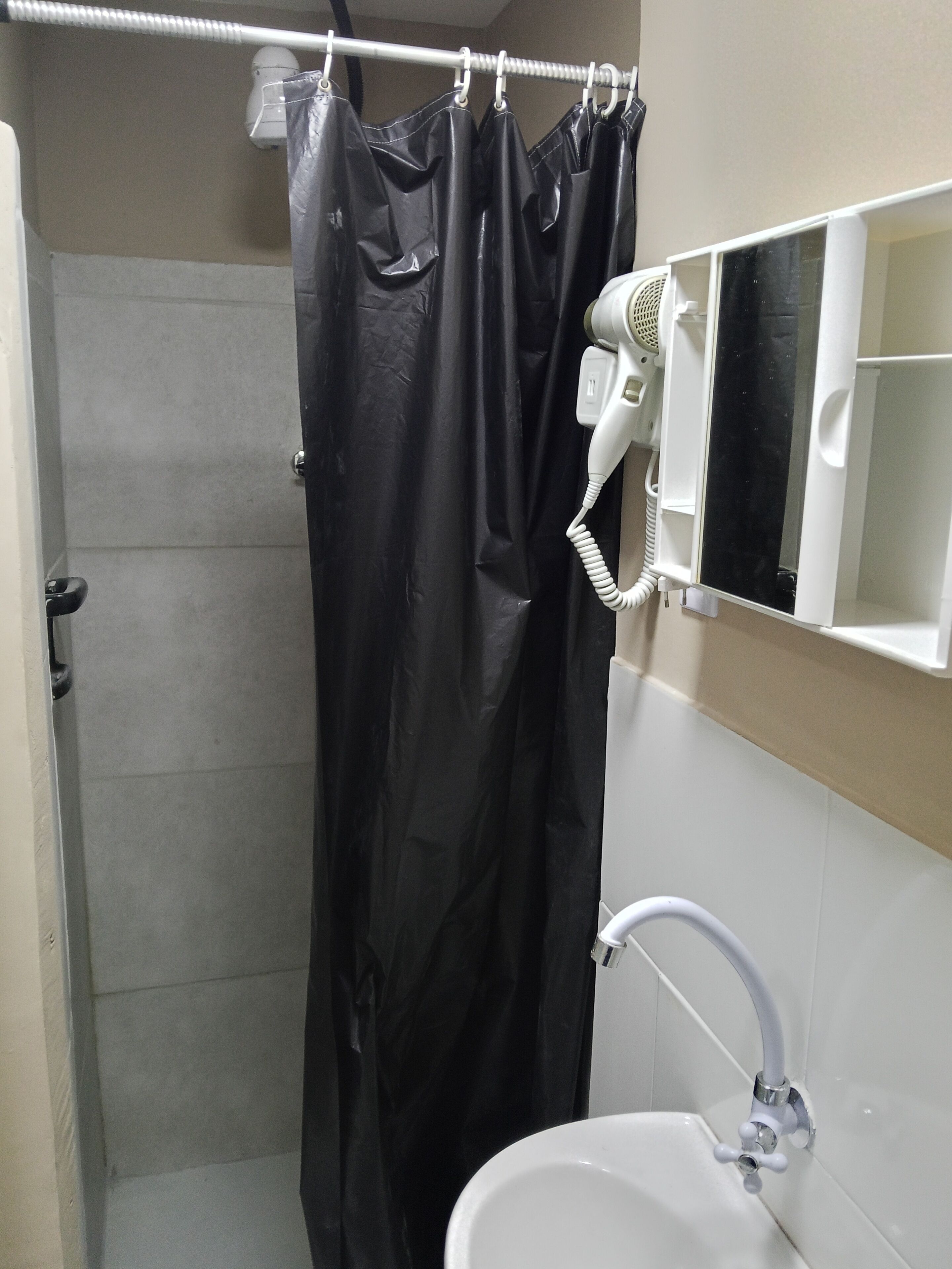Casa de banho com cortina de chuveiro, secador de cabelo e pia.