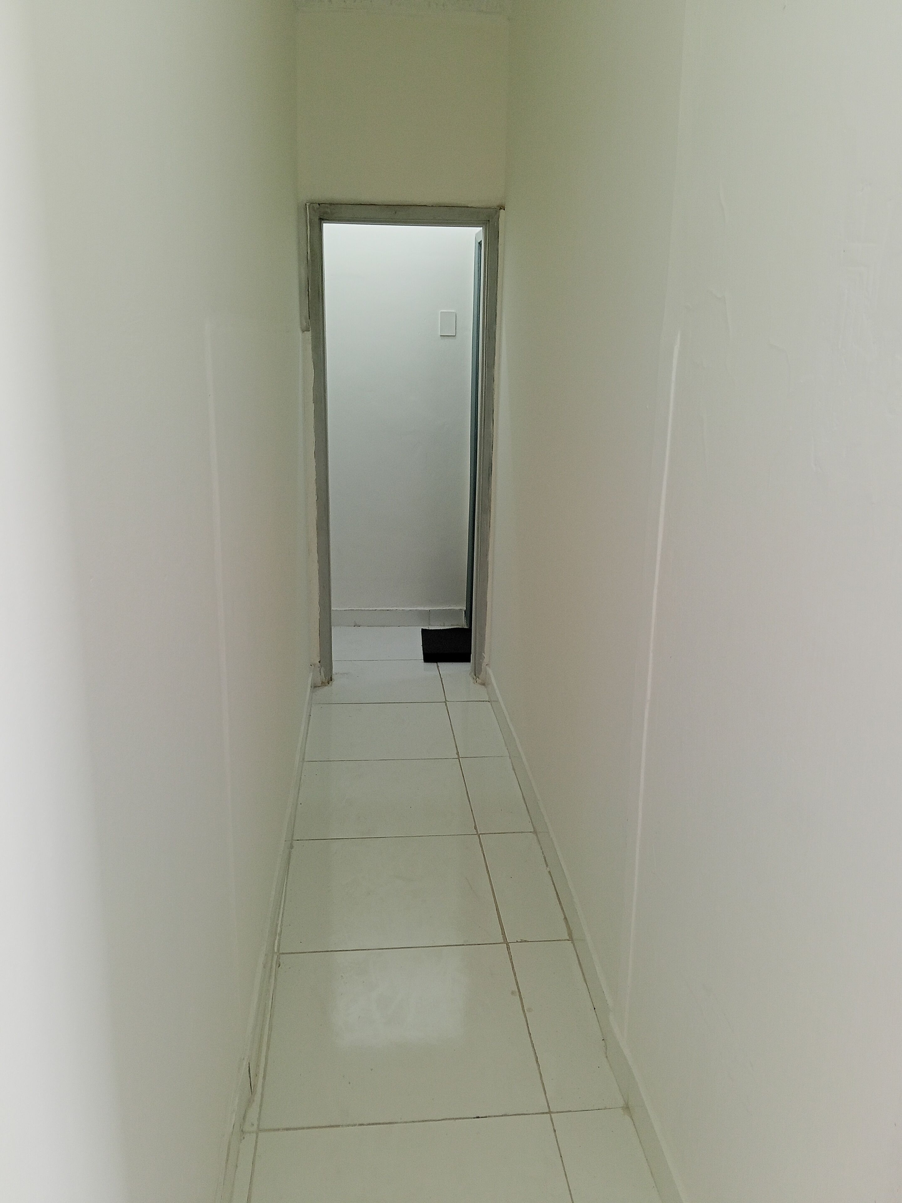 A narrow, tiled hallway with white walls and a door at the end.