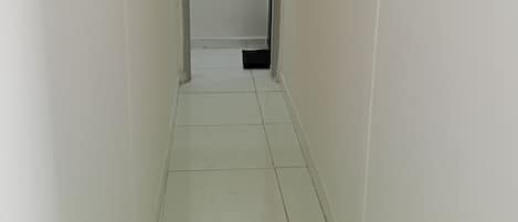 A narrow, tiled hallway with white walls and a door at the end.