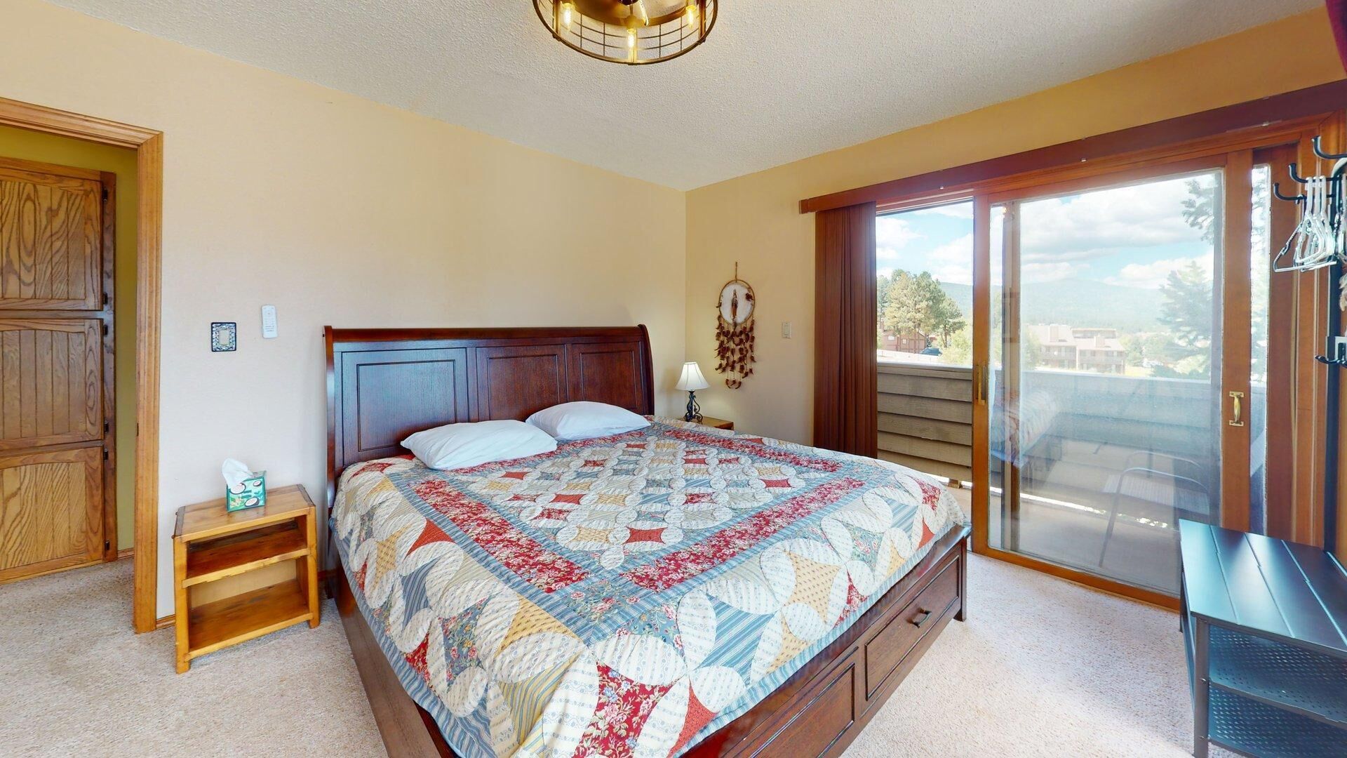 A bedroom with a bed, a nightstand, a dresser, a dreamcatcher, and a view of the outdoors.