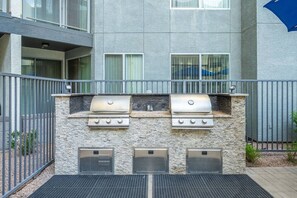 A barbecue grill setup with a stone wall and metal grill covers, located in an outdoor area with a metal fence. - Bright Tempe Studio • Green Views • 5 Min to A (Tempe)