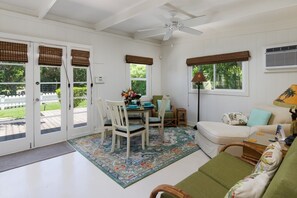 Una habitación con una mesa de comedor, sillas, un sofá, un ventilador de techo y un ventanal con vistas a zonas verdes.
