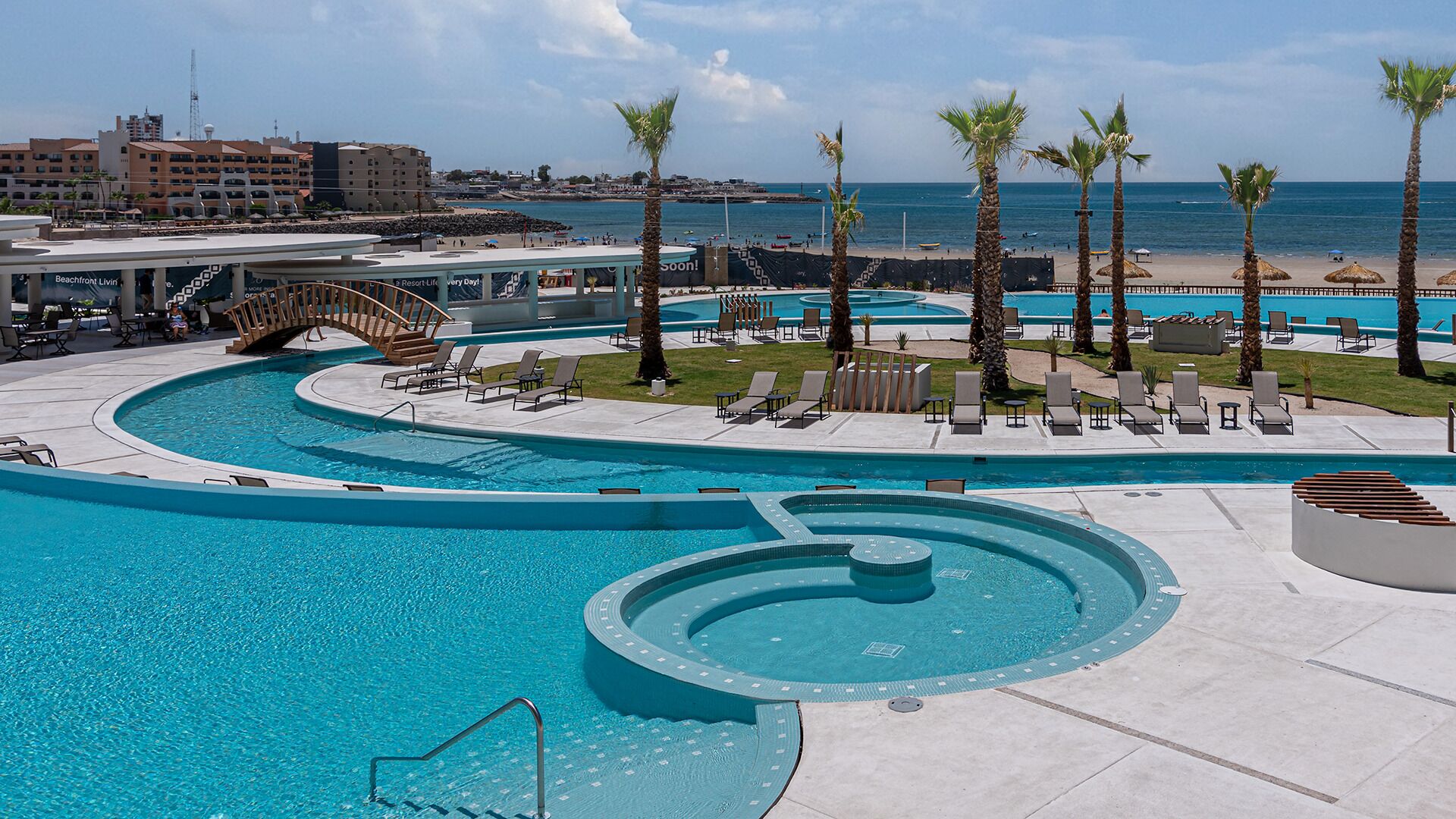A resort pool area with multiple swimming pools, lounge chairs, and palm trees.