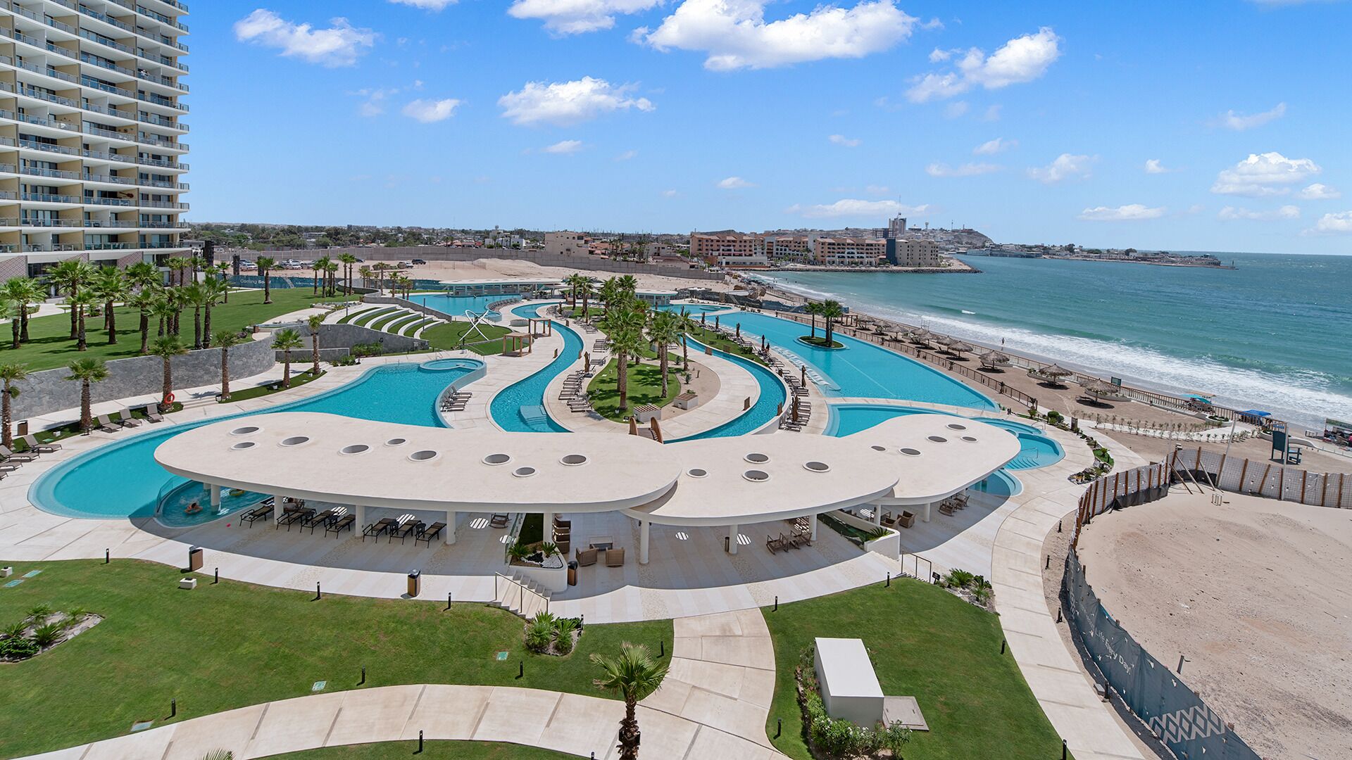 Een resort met een groot, kronkelend zwembad, een strand en uitzicht op de oceaan.