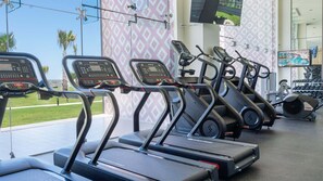 Une salle de sport équipée de tapis de course, dotée d’un murmiroir et offrant une vue sur l’océan.