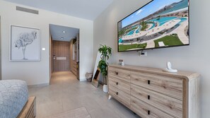 Une chambre d’hôtel dotée d’un grand téléviseur diffusant une vue sur le complexe hôtelier, d’une commode en bois, d’un lit et d’une œuvre d’art encadrée.
