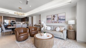 A modern living room with a sofa, two leather chairs, a coffee table, and a kitchen in the background. - Two 406 - Sea Luxe 1 bedroom condo (Puerto Peñasco)