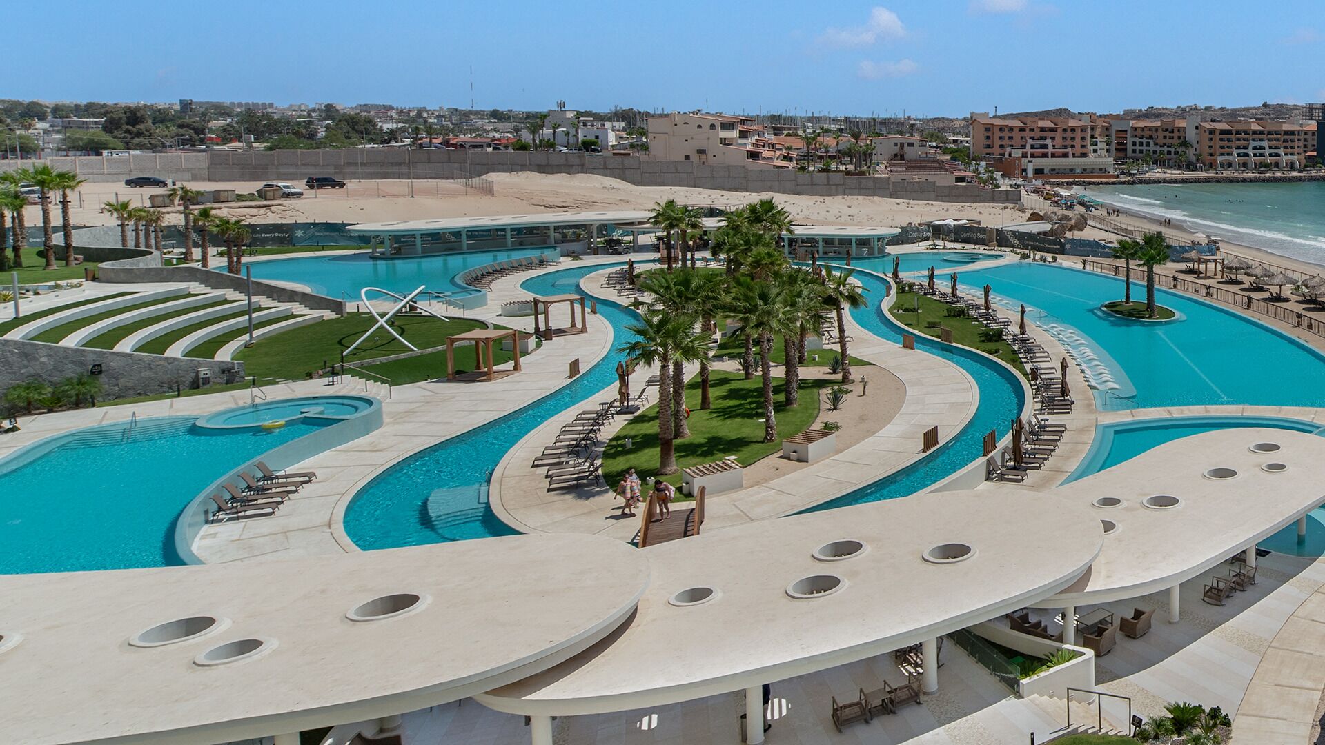 A resort with multiple swimming pools, palm trees, and a beach view.