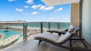 Un balcon avec vue sur une plage et l’océan, une chaise longue et une table avec des boissons.