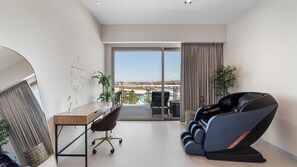 Une chambre d’hôtel moderne équipée d’un bureau, d’une chaise, d’un fauteuil de massage et offrant une vue sur une piscine et des bâtiments.