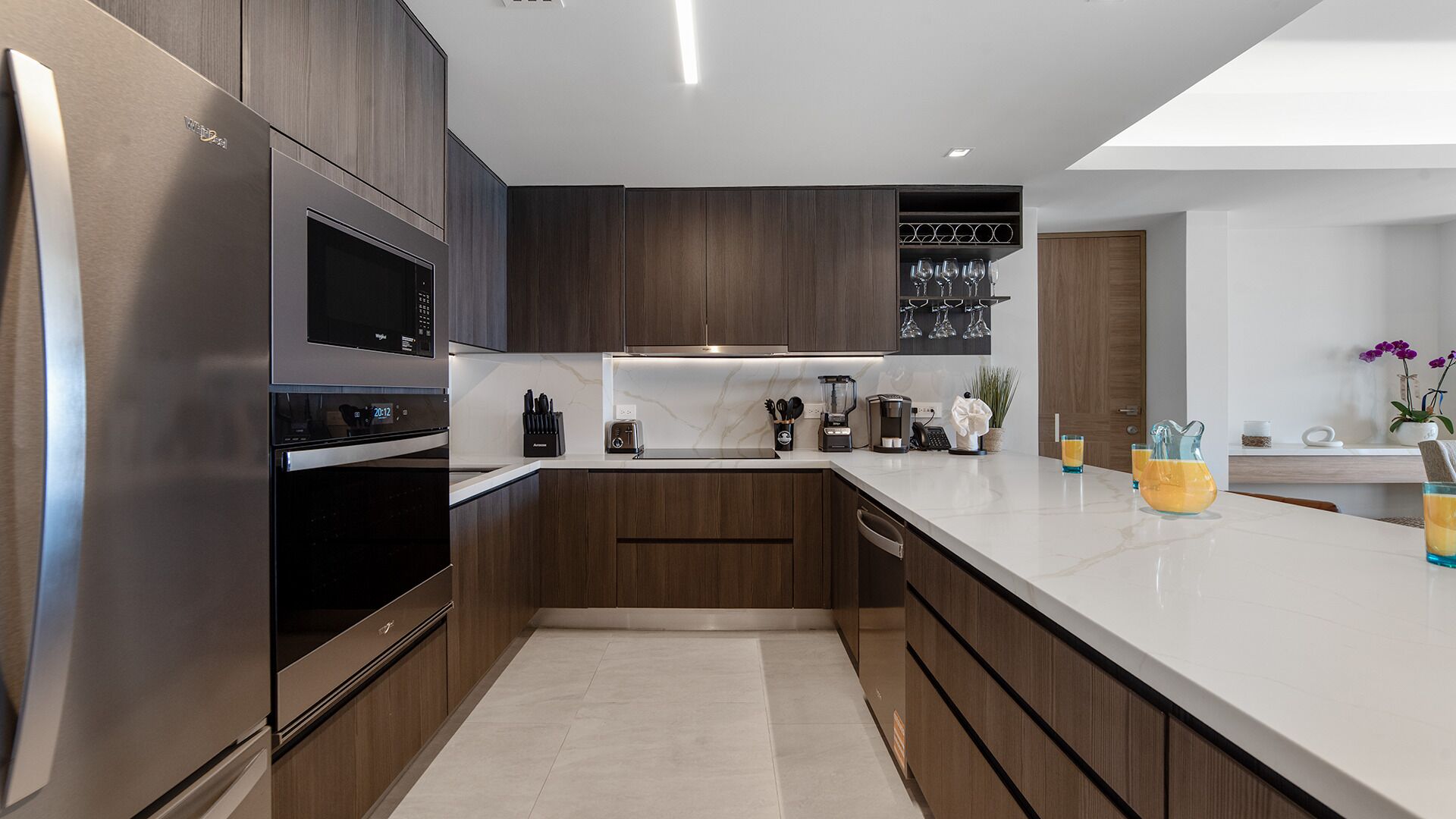 Une cuisine moderne avec des meubles en bois foncé, des appareils électroménagers en acier inoxydable et un plan de travail blanc.