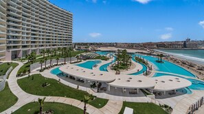 Ein Hotel mit mehreren Schwimmbecken, einem Strand und einer Stadtkulisse im Hintergrund.
