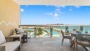 Ein Balkon mit Blick auf Pool und Strand, ausgestattet mit Tisch, Stühlen und einer Couch.