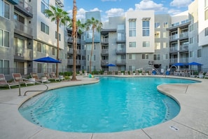 A swimming pool surrounded by modern apartment buildings with balconies, lounge chairs, and palm trees. - Chic Tempe Studio • Pool+Fast Wi-Fi • 5 Min to (Tempe)