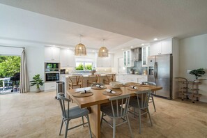 Een moderne keuken met witte kasten, een roestvrijstalen koelkast en een eethoek met een houten tafel en stoelen.