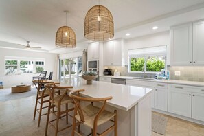 A modern kitchen with white cabinetry, a central island with bar stools, and pendant lighting. - Latitude Adjustment by SeaBreeze Vacation (Holmes Beach)