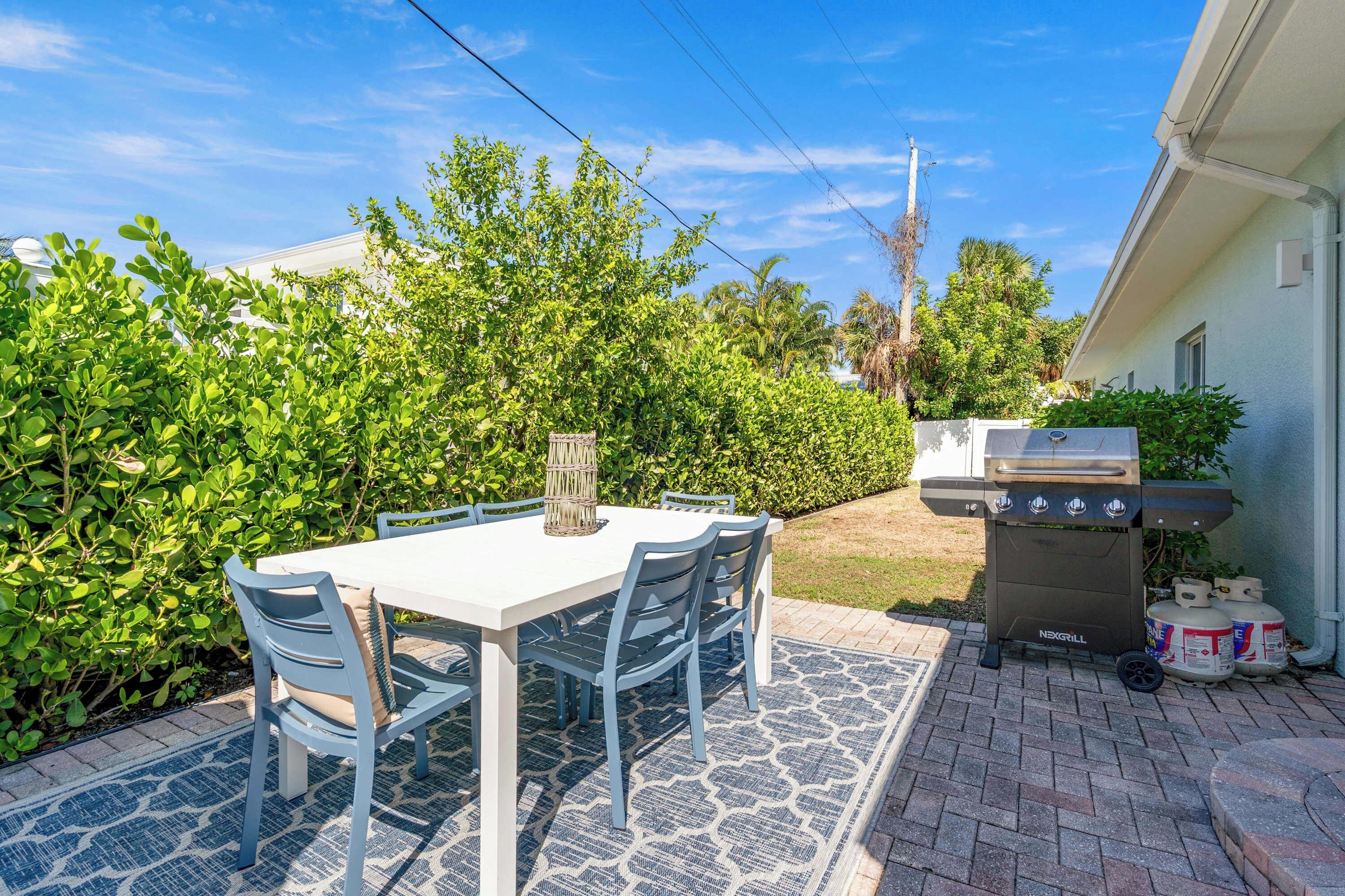Une terrasse avec une table et des chaises, un barbecue et une haie.