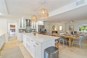 A spacious kitchen with white cabinetry, a central island, and a dining area with a wooden table and chairs. - Latitude Adjustment by SeaBreeze Vacation (Holmes Beach)