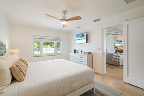 Een slaapkamer met een bed, een dressoir, een televisie en een plafondventilator.