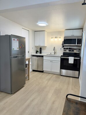 Cozinha moderna com eletrodomésticos de aço inoxidável, armários brancos e piso de madeira.