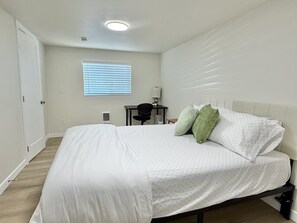 A bedroom with a bed, a desk, a chair, and a window with blinds.
