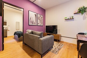 A modern living room with a grey sofa, a flat-screen TV, wooden flooring, and a small dining area. - Suite | Polanco | Relax (Ciudad de México)