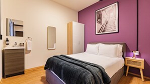 A bedroom with a bed, a wardrobe, a mirror, a nightstand, and a wall-mounted picture.
