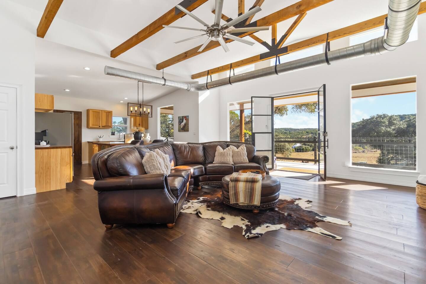 A spacious living room with a large leather sectional sofa, a cowhide rug, and a ceiling fan.
