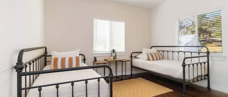 A bedroom with two beds, a ceiling fan, a window with blinds, and a wooden floor.