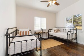 A bedroom with two beds, a ceiling fan, a window with blinds, and a wooden floor. - 2 Homes on Boerne Acreage w/ Fire Pit & Hill Views (Boerne)