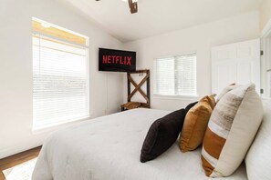 Quarto com cama, TV fixada na parede exibindo 'NETFLIX' e um cabideiro de madeira.