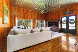 A living room with a sofa, wooden walls, a ceiling fan, and a fireplace with a Netflix sign. - 2 Homes on Boerne Acreage w/ Fire Pit & Hill Views (Boerne)